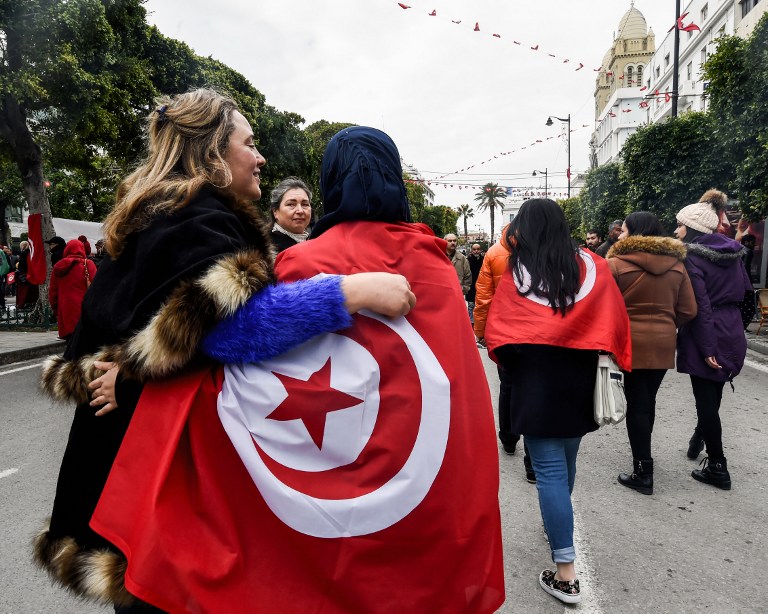 Two Tunisian women embrace as one wears the national flag, during a rally on January 14, 2017 in the Habib Bourguiba Avenue in the capital Tunis to mark the sixth anniversary of the 2011 revolution. / AFP PHOTO / FETHI BELAID