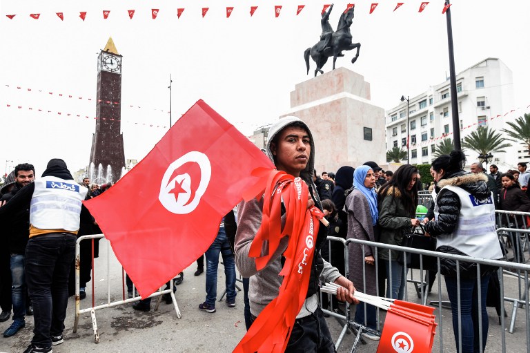 A Tunisian peddlar selling national flag crosses a police roadblock on his way to a rally on January 14, 2017 in the Habib Bourguiba Avenue in the capital Tunis marking the sixth anniversary of the 2011 revolution. / AFP PHOTO / FETHI BELAID